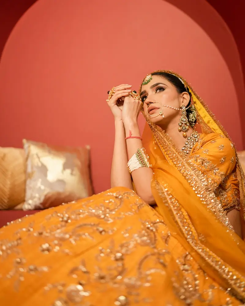 A bride in a saffron lehenga reclines against a terracotta wall