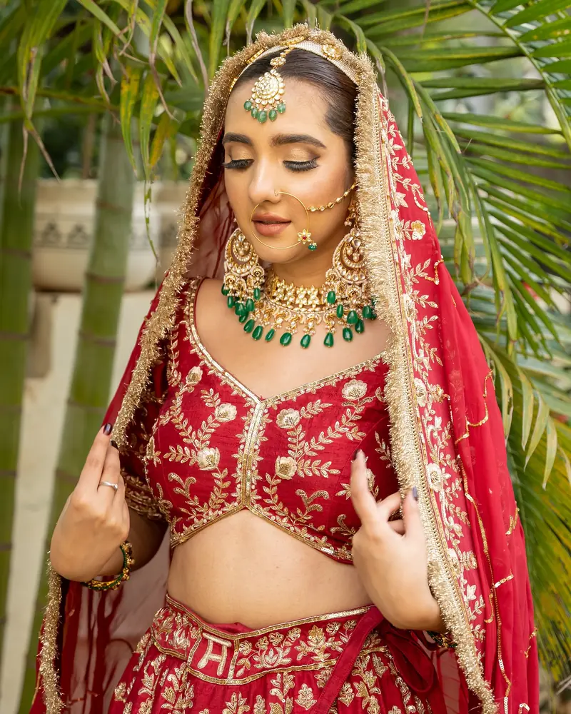 A bride in red and emerald jewellery photographed through soft green leaves