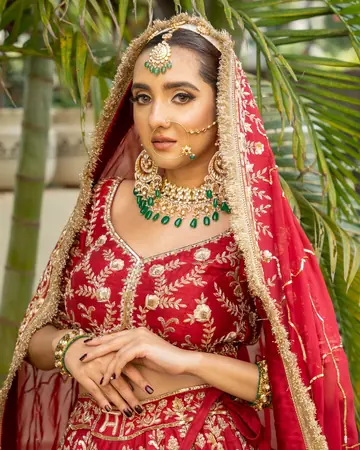 The bride in a red lehenga with hands folded, palms behind her
