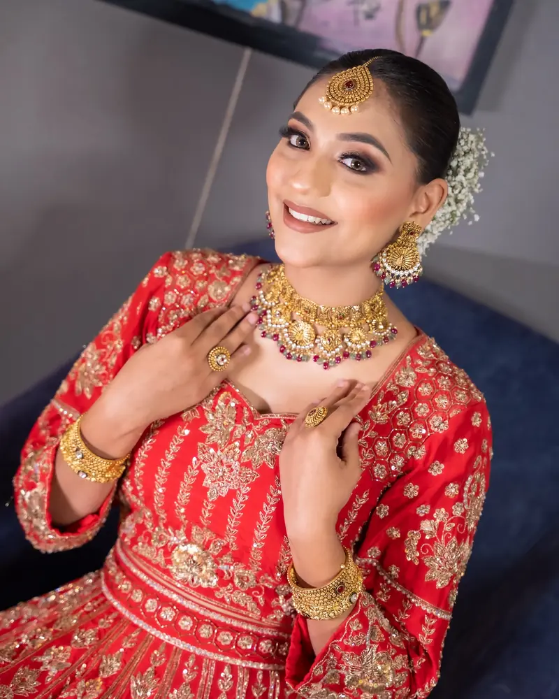 A bride in red smiles, hands framing her gold choker