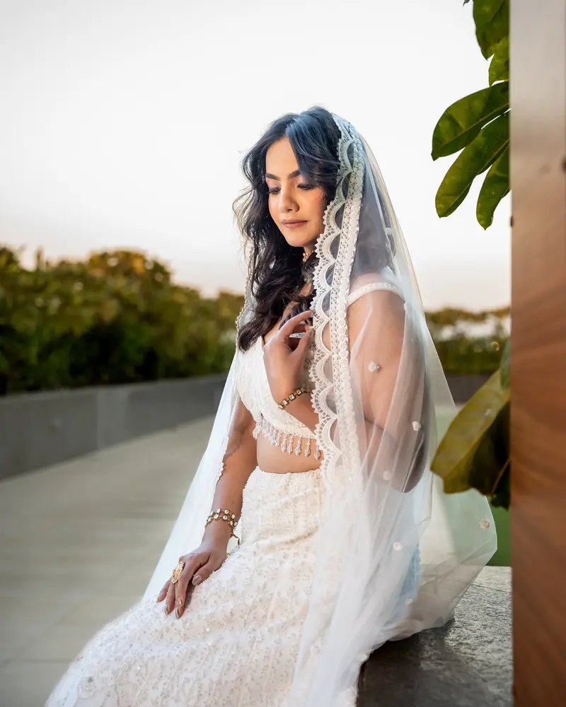 A bride in white holds the edge of a lace veil at golden hour
