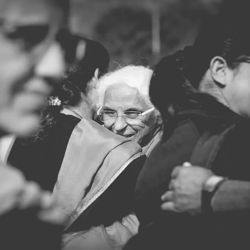 Black-and-white photograph of an elderly woman smiling as family lean in around her