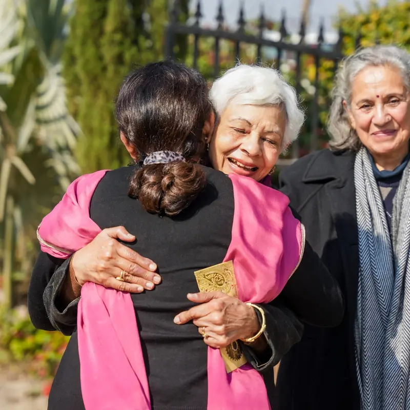 A grandmother hugs a guest tightly in the winter sun, laughing