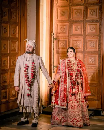 Gauri and her groom hold hands in front of tall carved wooden doors