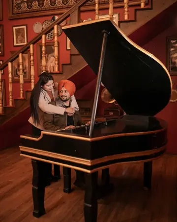 The couple laughing at a grand piano in a red, portrait-lined room