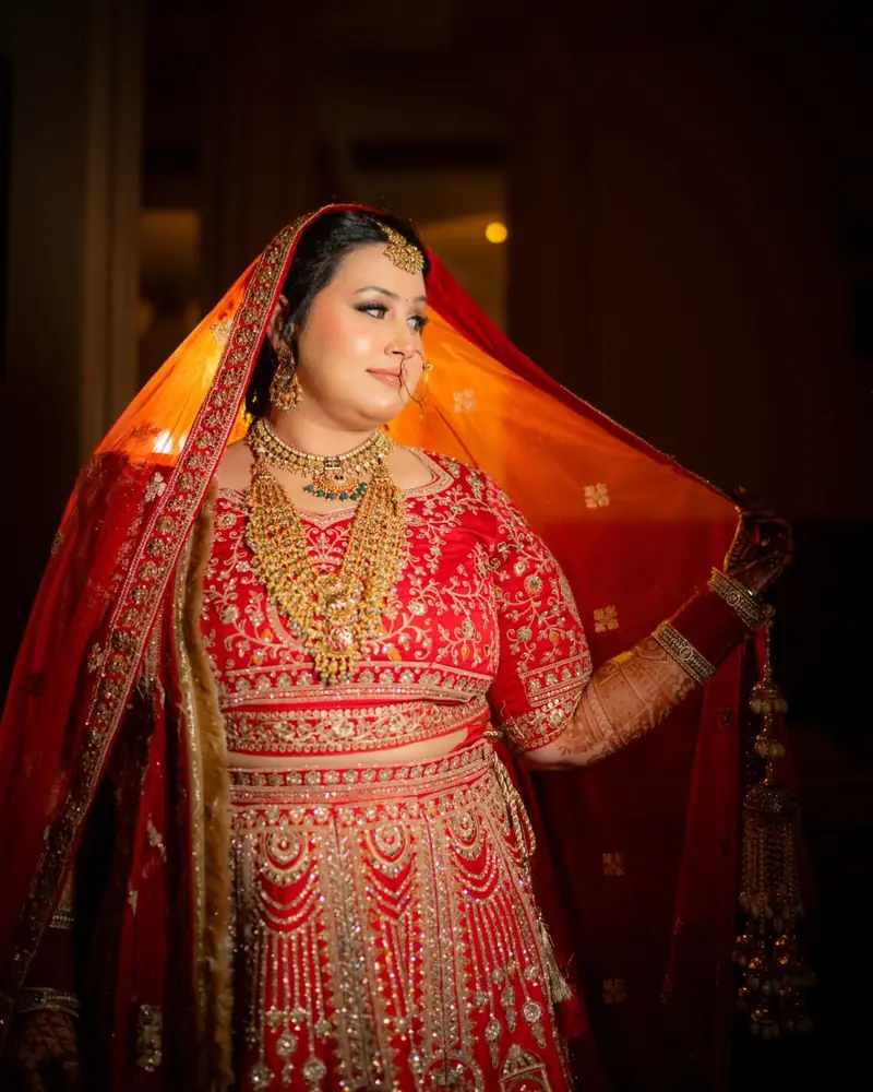 Gauri lifts her red dupatta, warm light glowing through the fabric