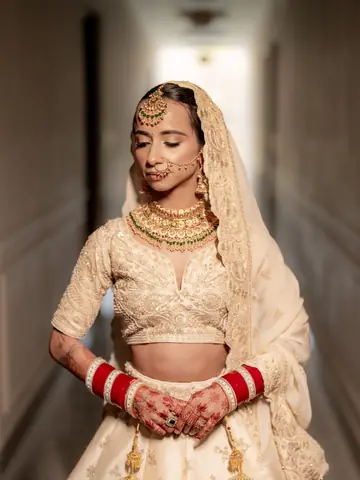 Mukta in ivory with red chooda, hands folded, in a quiet corridor
