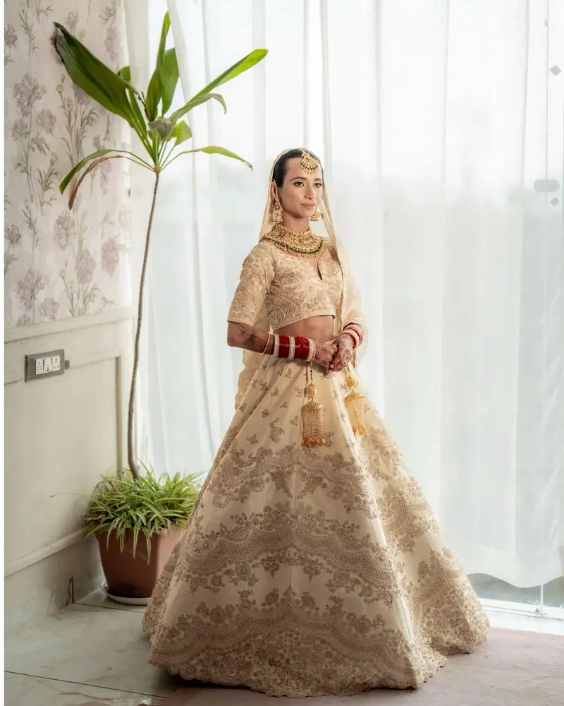 Mukta in an ivory and gold lehenga turns toward a bright, curtained window