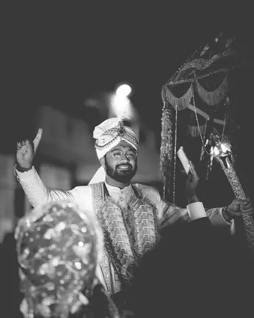 Black-and-white photograph of the groom dancing at his baraat, hand raised