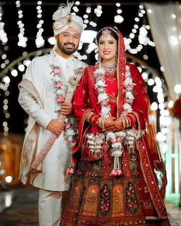 Pransh and Gunjan in wedding clothes and garlands, standing before a wall of lights