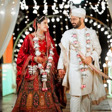 Gunjan and Pransh walk hand in hand under an arch of lights, both smiling