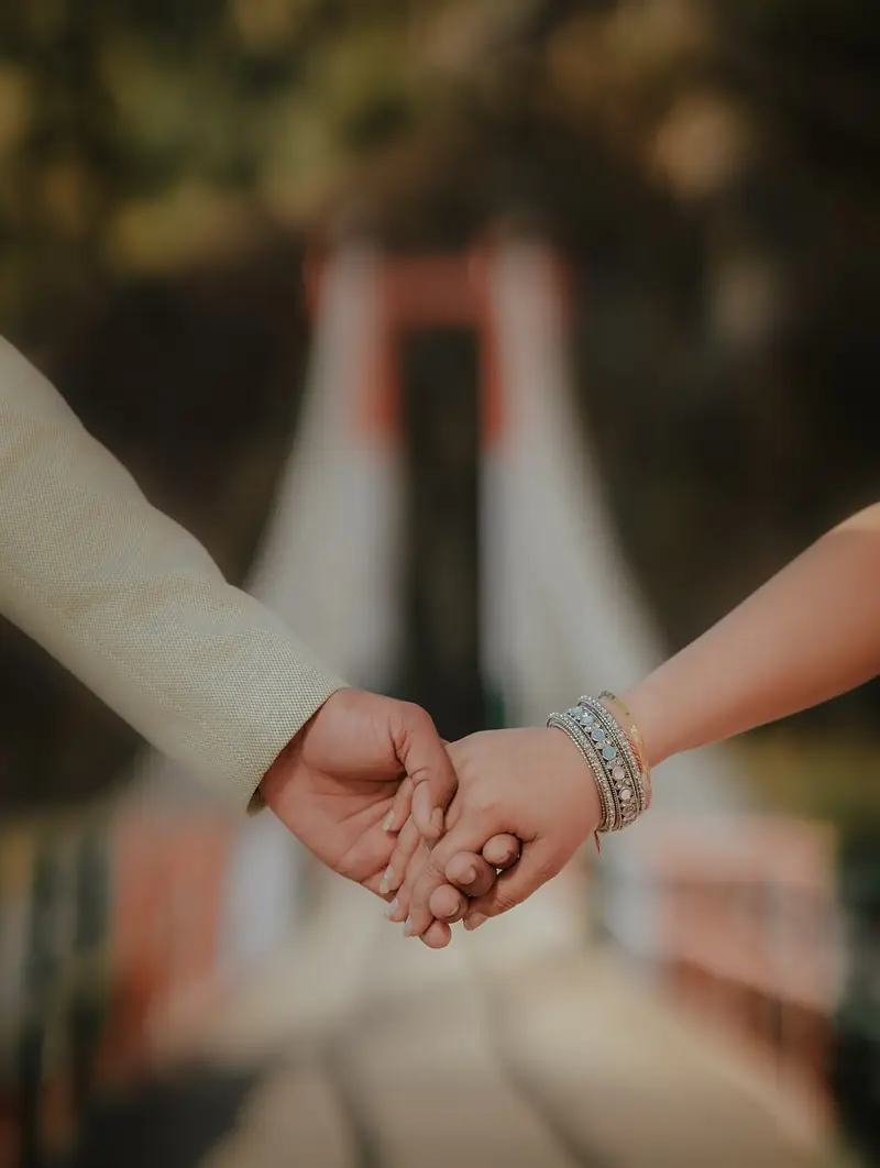 Close-up of the couple's joined hands, the bridge soft and blurred behind