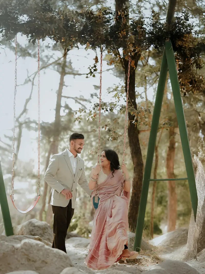 A couple laughing by a swing among tall pine trees, soft mountain light