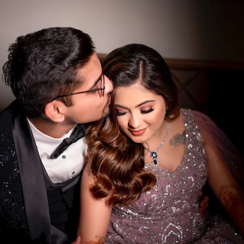 Groom in a tuxedo kisses his bride's cheek; she smiles with her eyes closed