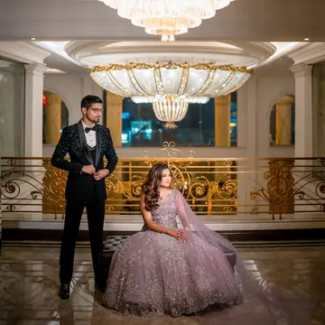 Bhavya seated in a lilac gown and Vaibhav in a tuxedo, beneath a crystal chandelier